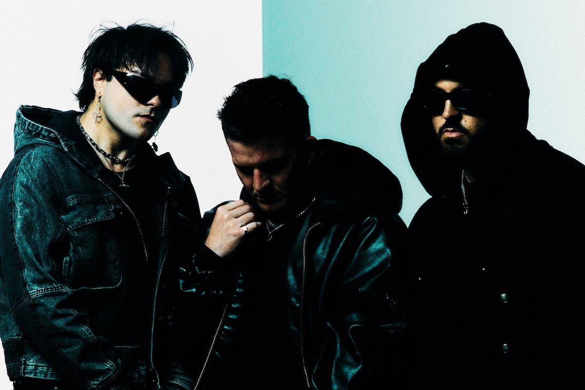 Band members of Banks Arcade pose in dark jackets against a split white and light blue background, two wearing sunglasses and one wearing a hood.